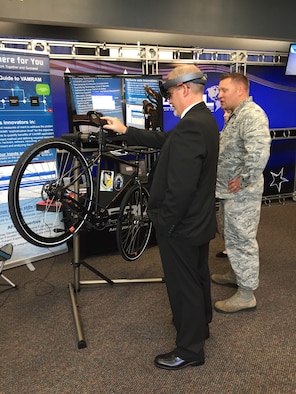 Dr. Michael Gregg (left), director of the Air Force Research Laboratory Aerospace Systems Directorate, uses a mixed-reality application to change the tire on a Wright Cycle Company bicycle as Capt. David Eisensmith guides the process. The demonstration, on display at the 2019 Air Vehicles Technology Symposium, is part of the Virtual, Augmented, and Mixed Reality for Aircraft Maintenance team’s effort to show the technology’s potential for future aircraft maintenance. (U.S. Air Force Photo)