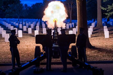 Soldiers fire a cannon at a cemetery at night.