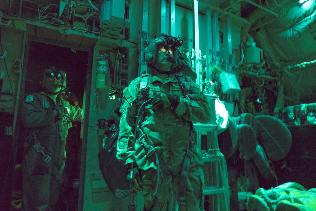 Two airmen look intensely though binoculars while standing in a green lit area.