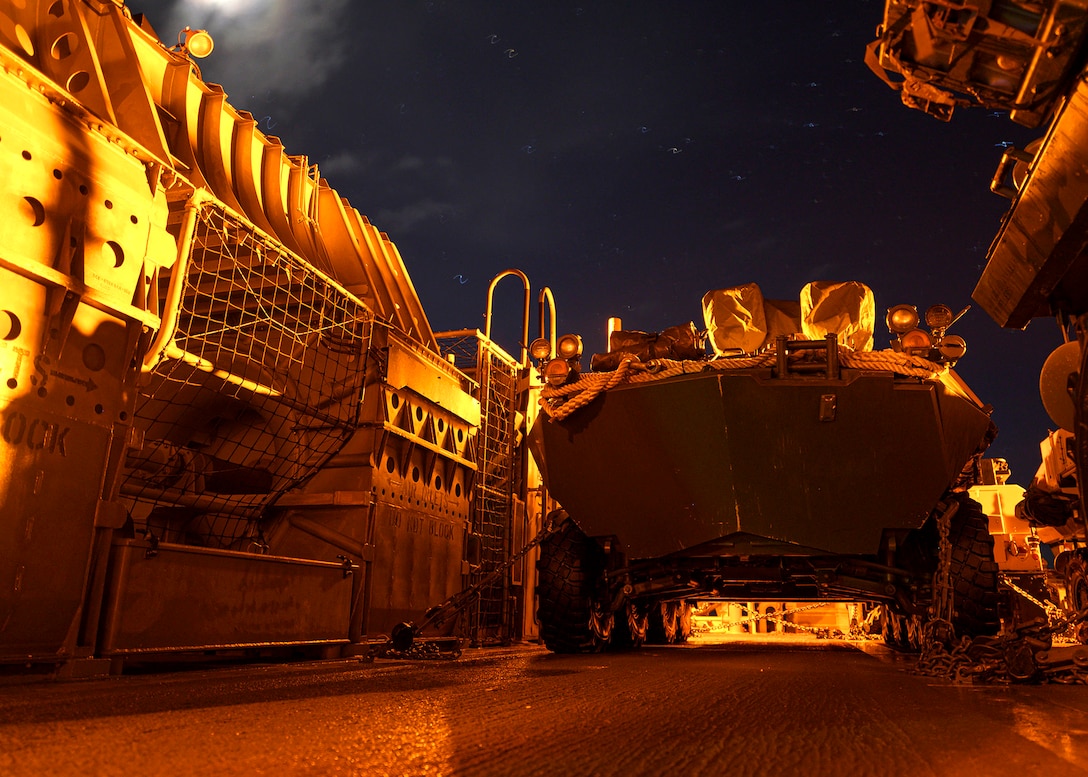 A large military vehicle sits in a lit landing dock.