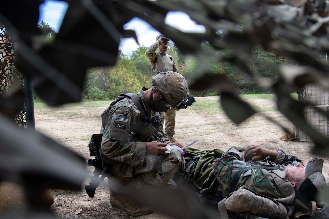 A soldier kneels on the ground to evaluate another soldier.