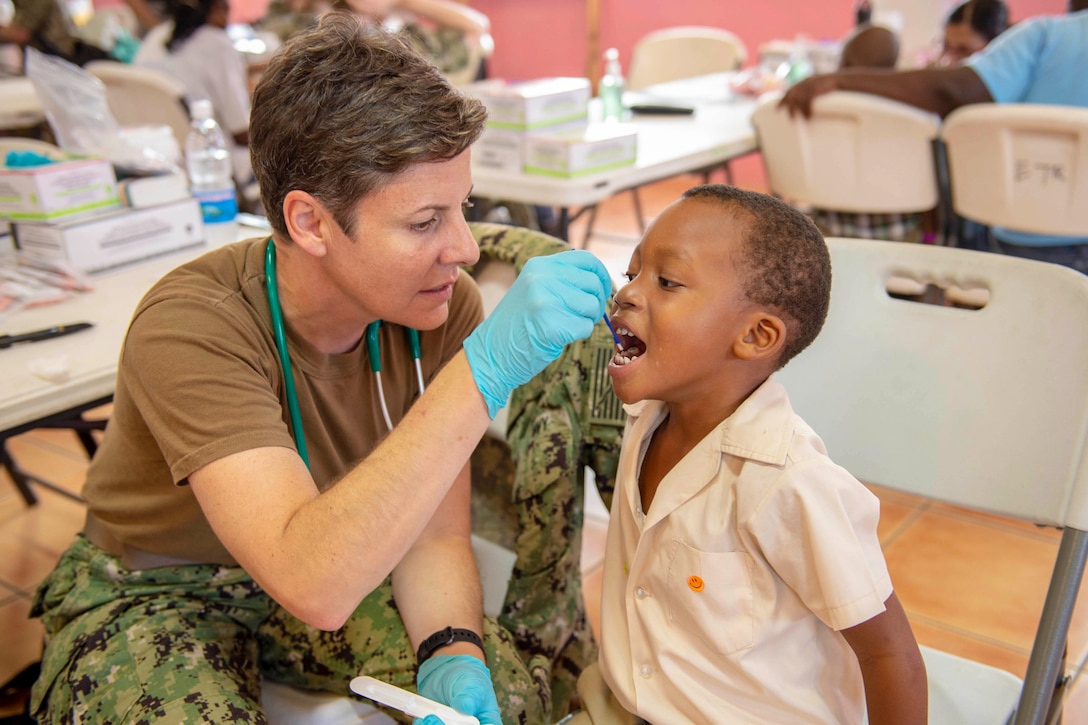 A sailor uses a tool to clean the teeth of a child.