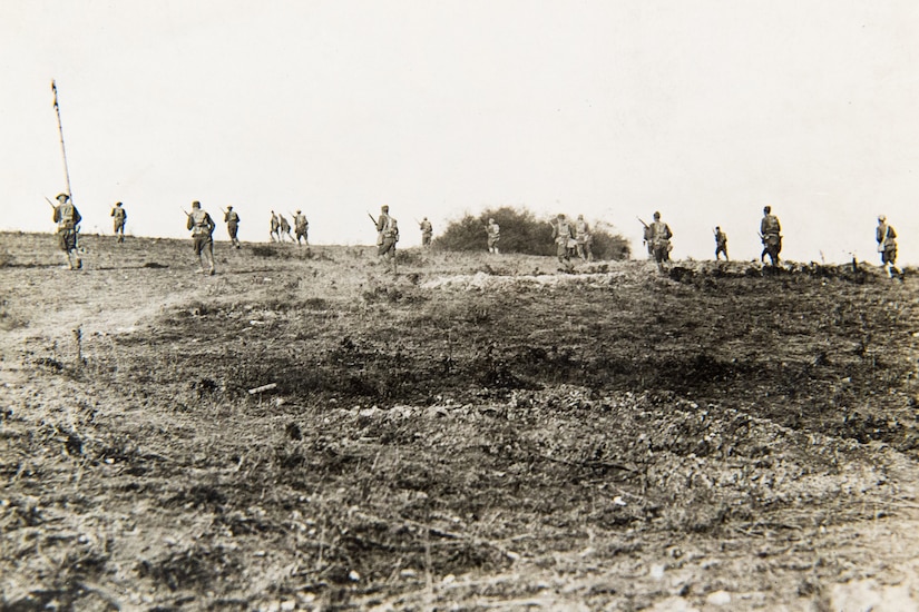 Several soldiers in the distance run away from the camera in what appears to be a burned-out, barren wasteland.
