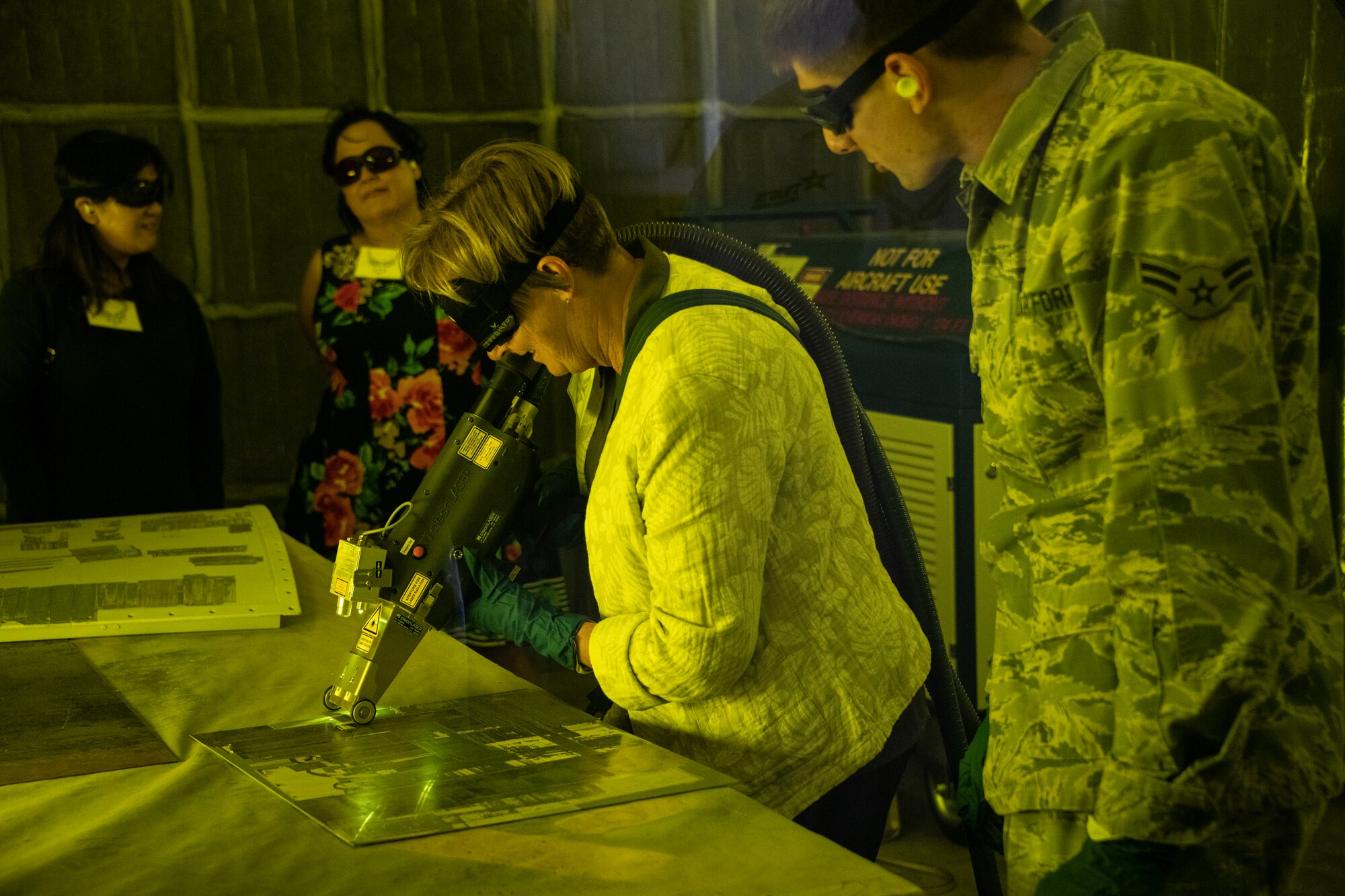 U.S. Air Force Airman 1st Class Rick Comps, right, 60th Aircraft Maintenance Squadron aircraft structural maintenance craftsman, observes Honorary Commander Pat Shamansky, Fairfield-Suisun School District, use a laser to remove paint during the 60th Maintenance Group Honorary Commanders tour, Oct. 4th, 2019, at Travis Air Force Base, California.  The purpose of the Honorary Commanders Program is to promote relationships between base senior leadership and civilian partners, foster civic appreciation of the Air Force mission and its Airmen, maximize opportunities to share the Air Force story with new stewards and to communicate mutual interest, challenges and concerns senior leaders and civilian stakeholders have in common. (U.S. Air Force photo by Heide Couch)