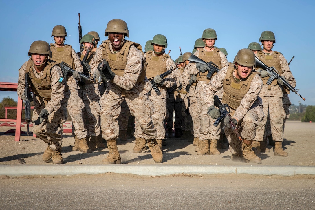 Marines in helmets wielding rifles charge forward on an outdoor course while yelling.