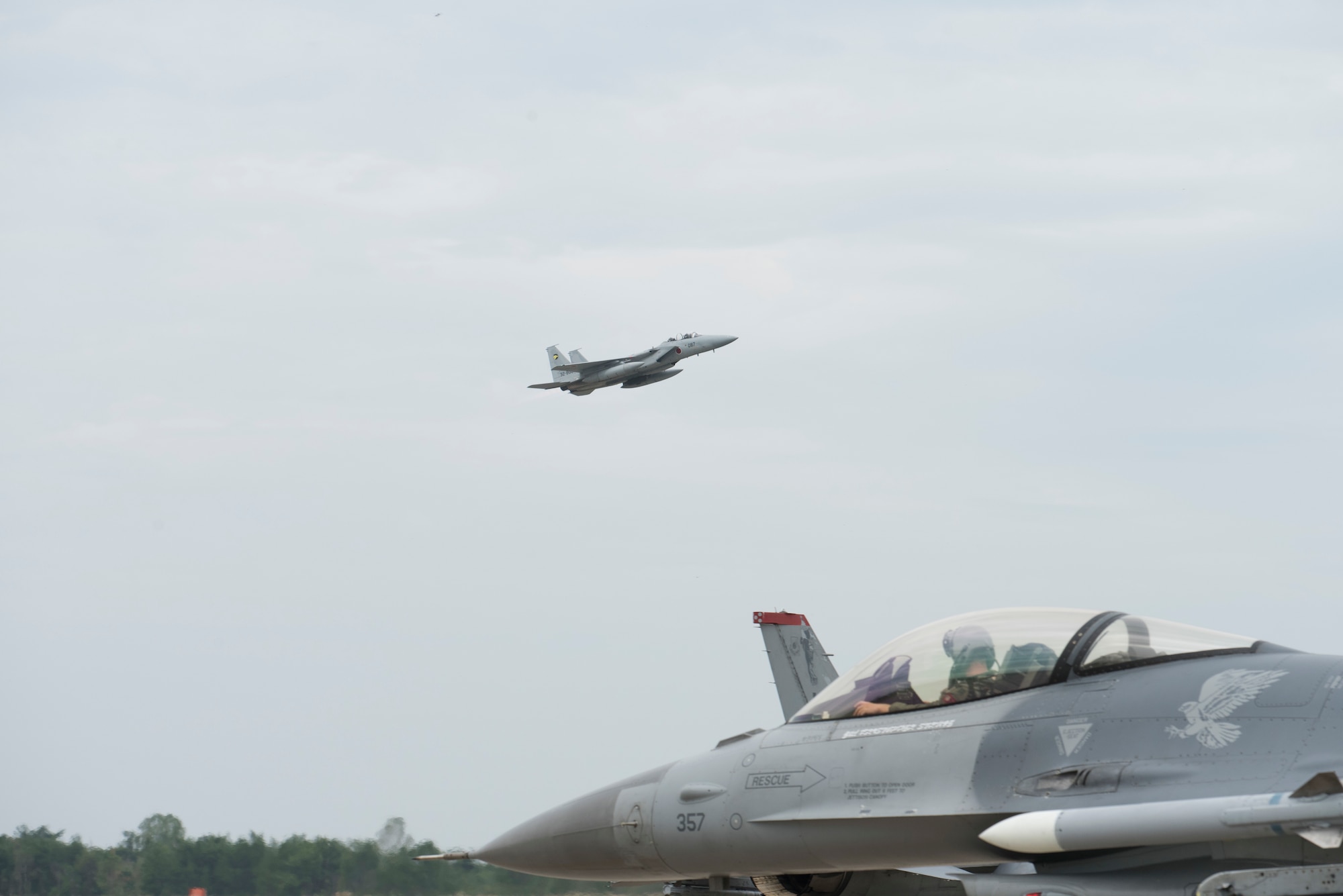 A Mitsubishi F-15J flies above a taxiing F-16 Fighting Falcon during an aviation training relocation at Komatsu Air Base, Japan, Oct. 2, 2019. The 28 stories executed during the ATR gave Wild Weasel’s the ability to learn, train and integrate with their host nation partners while identifying successes and shortfalls. The F-15J is assigned to the 6th Air Wing Maintenance Squadron, Komatsu AB, and the F-16 is assigned to the 35th Maintenance Squadron from Misawa AB. (U.S. Air Force photo by Senior Airman Collette Brooks)