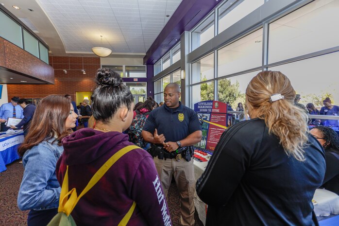 Joseph Carroll, Marine Corps Police Officer, speaks with three young women about career opportunities aboard Marine Corps Logistics Base Barstow during the Career and Education Expo at Barstow Community College, Barstow, Calif., Oct. 3.