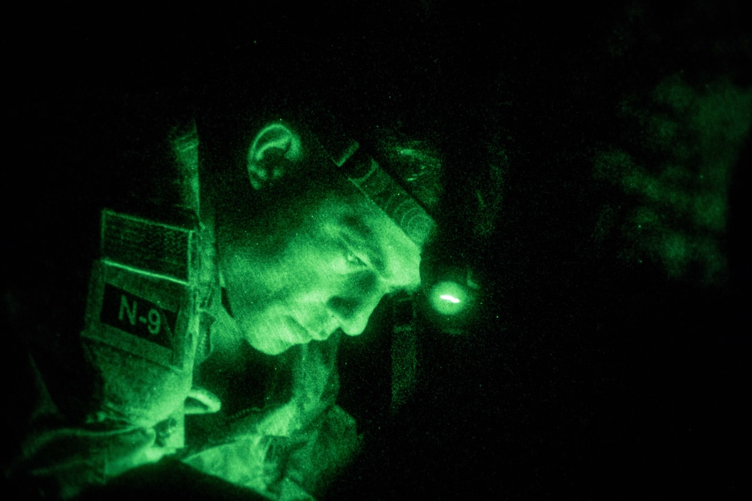 A soldier wearing a headlight is seen through night vision.