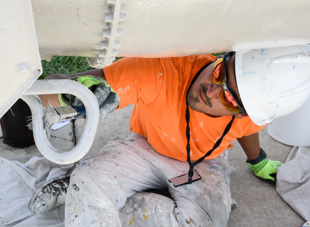 Jonathan Finn paints part of a TF-30 engine that is on display in front of the Engine Test Facility, Aug. 9, at Arnold Air Force Base. (U.S. Air Force photo by Jill Pickett) (This image has been altered by obscuring a badge for security purposes.)