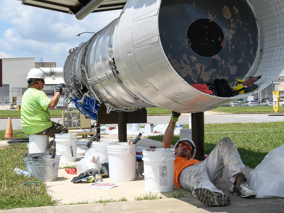 AEDC team members Jamie Elam, left, and Jonathan Finn, apply a fresh coat of paint Aug. 9 to a TF-30 engine on display in front of the Engine Test Facility at Arnold Air Force Base. The engine, tested in the ETF in the 1960s, was the first afterburner turbofan engine. The F-111 Aardvark, a multipurpose tactical fighter bomber retired from U.S. service in 1996, was powered by two TF-30 engines, and could fly at supersonic speeds. (U.S. Air Force photo by Jill Pickett) (This image has been altered by obscuring items for security purposes.)