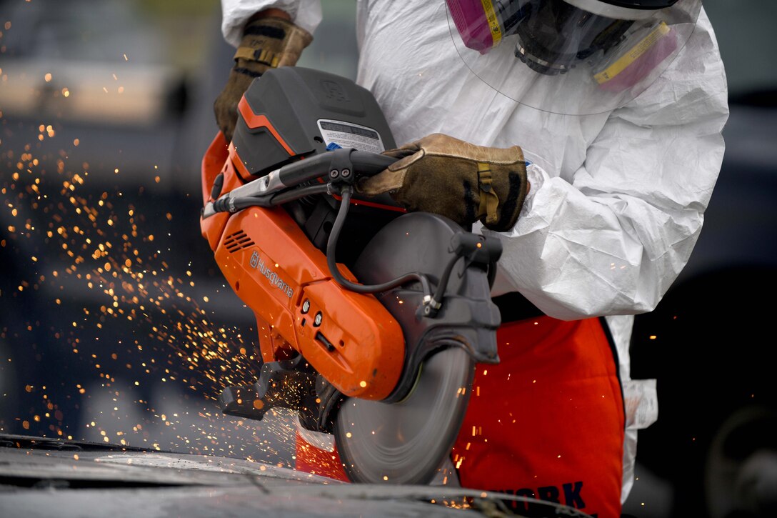 An airman uses a saw to cut int the hood of a car.