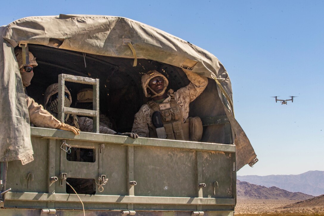 Marines in the back of a vehicle watch as an aircraft approaches.