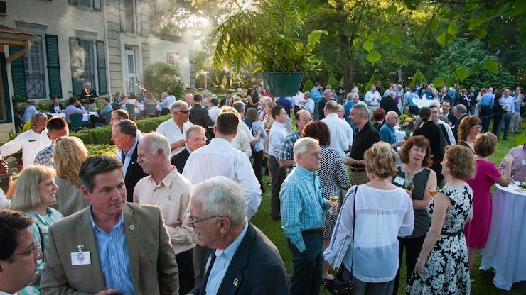 A large crowd of people talk in a well-lit evening garden party.