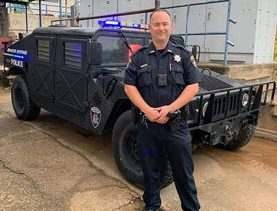 Police officer stands in front of Humvee.