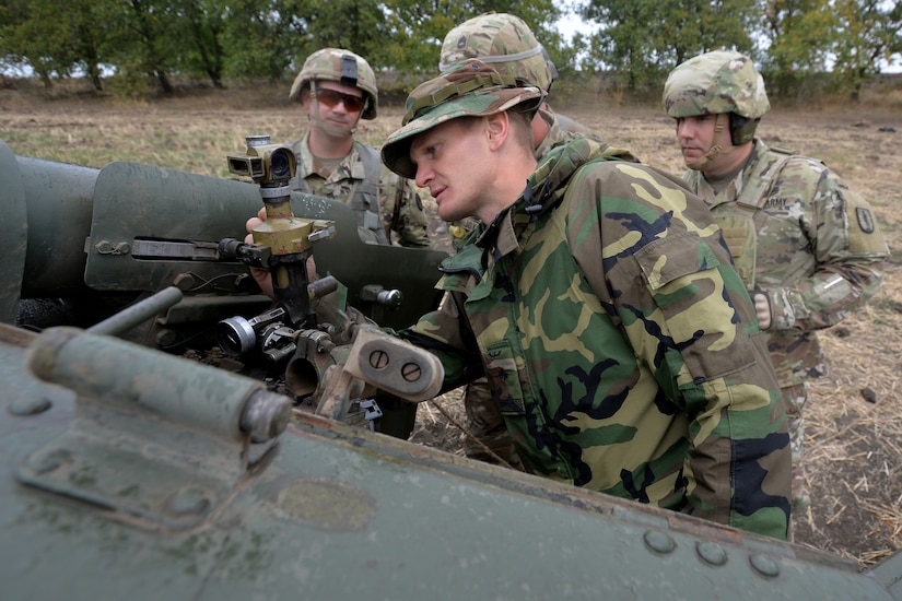One soldier examines an artillery piece as three others look on.