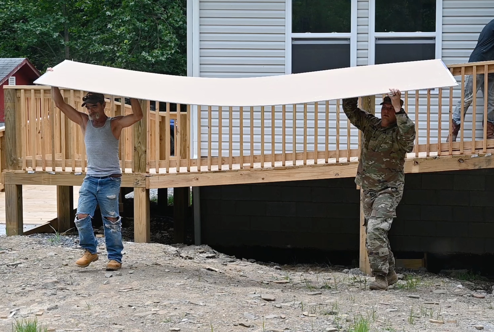Soldier and contractor carrying lumber at a job construction site.