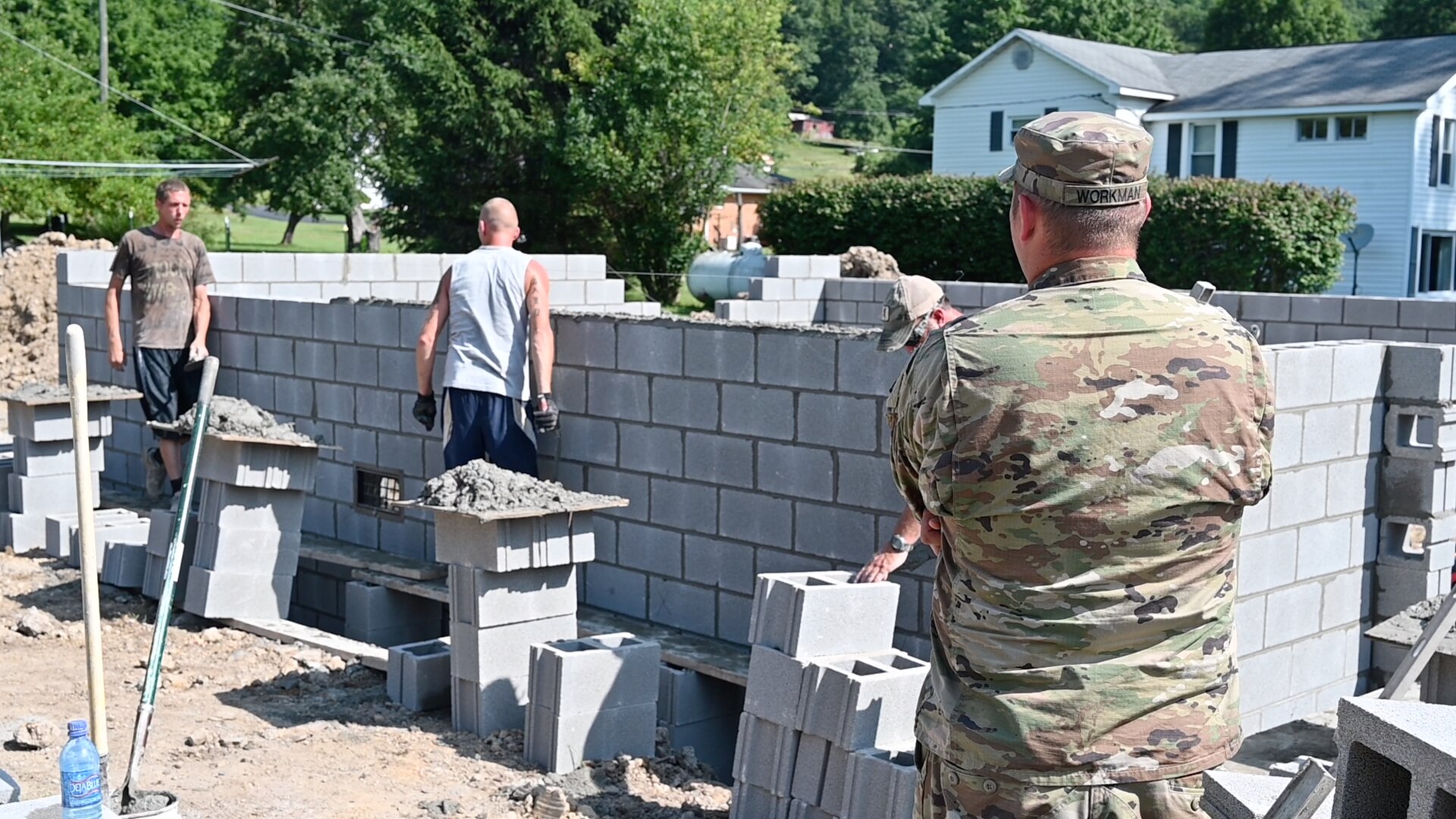 Soldier observing construction of a cinderblock home.