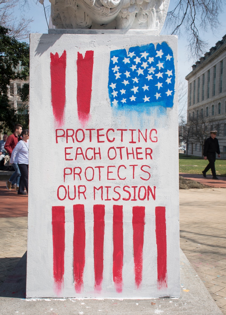 A red, white and blue painting of a stylized vertical U.S. flag superimposed by text reading, “protecting each other protects our mission.”