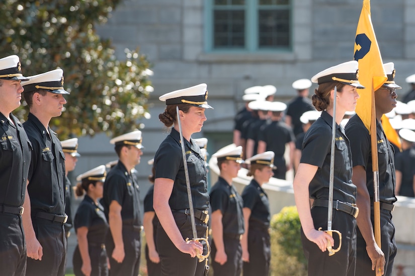 Sailors carrying swords march in formation.