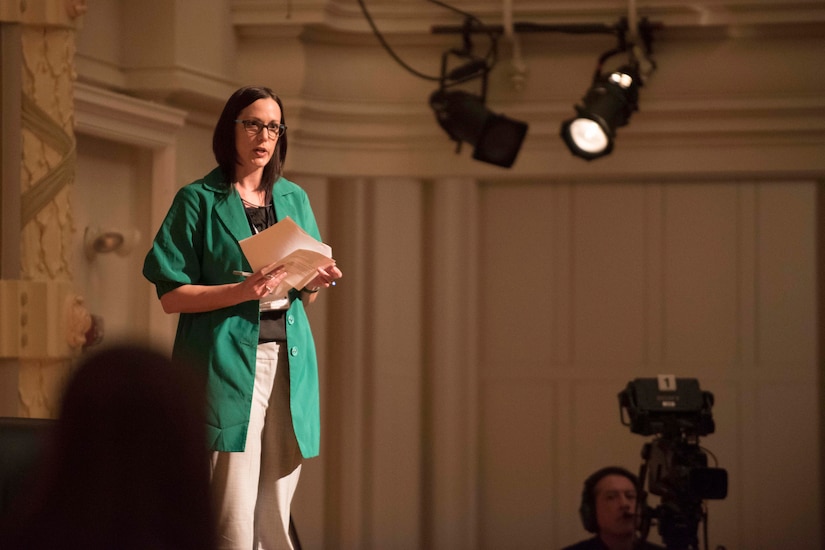 A woman speaks to an audience from a stage.