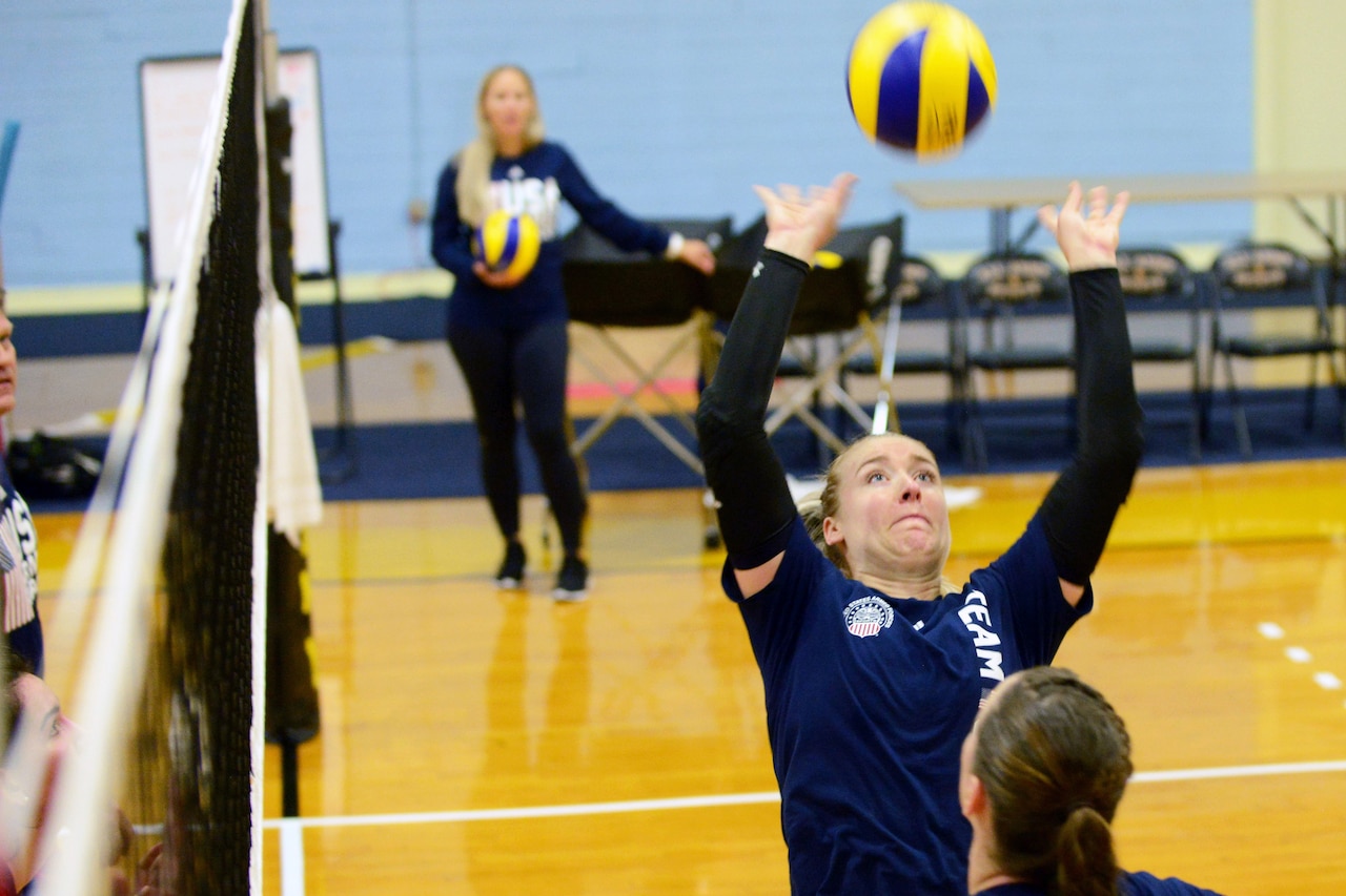 Woman jumps with both arms extended over her head to hit a volleyball.