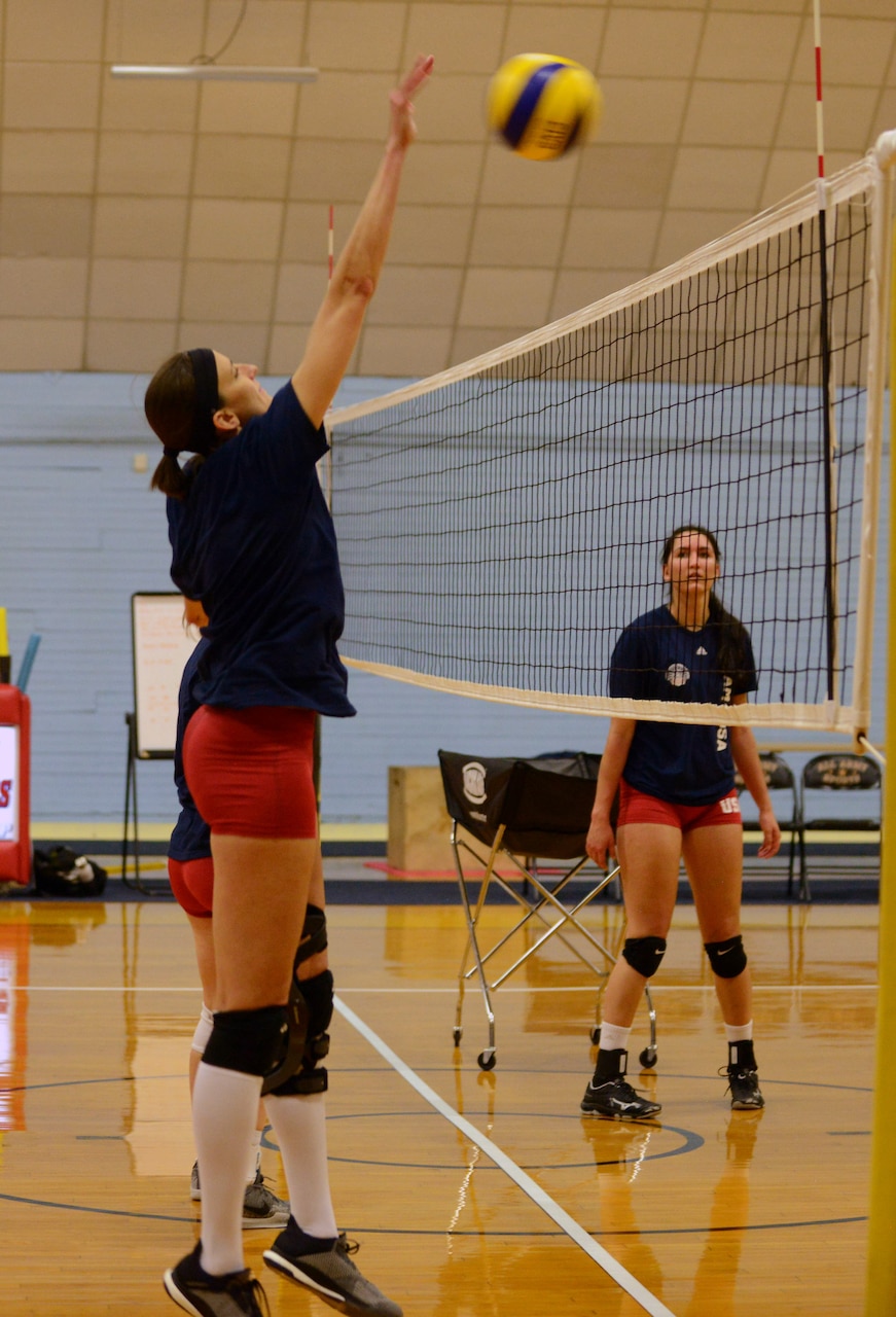 Woman jumps with both arms extended over her head to hit a volleyball.