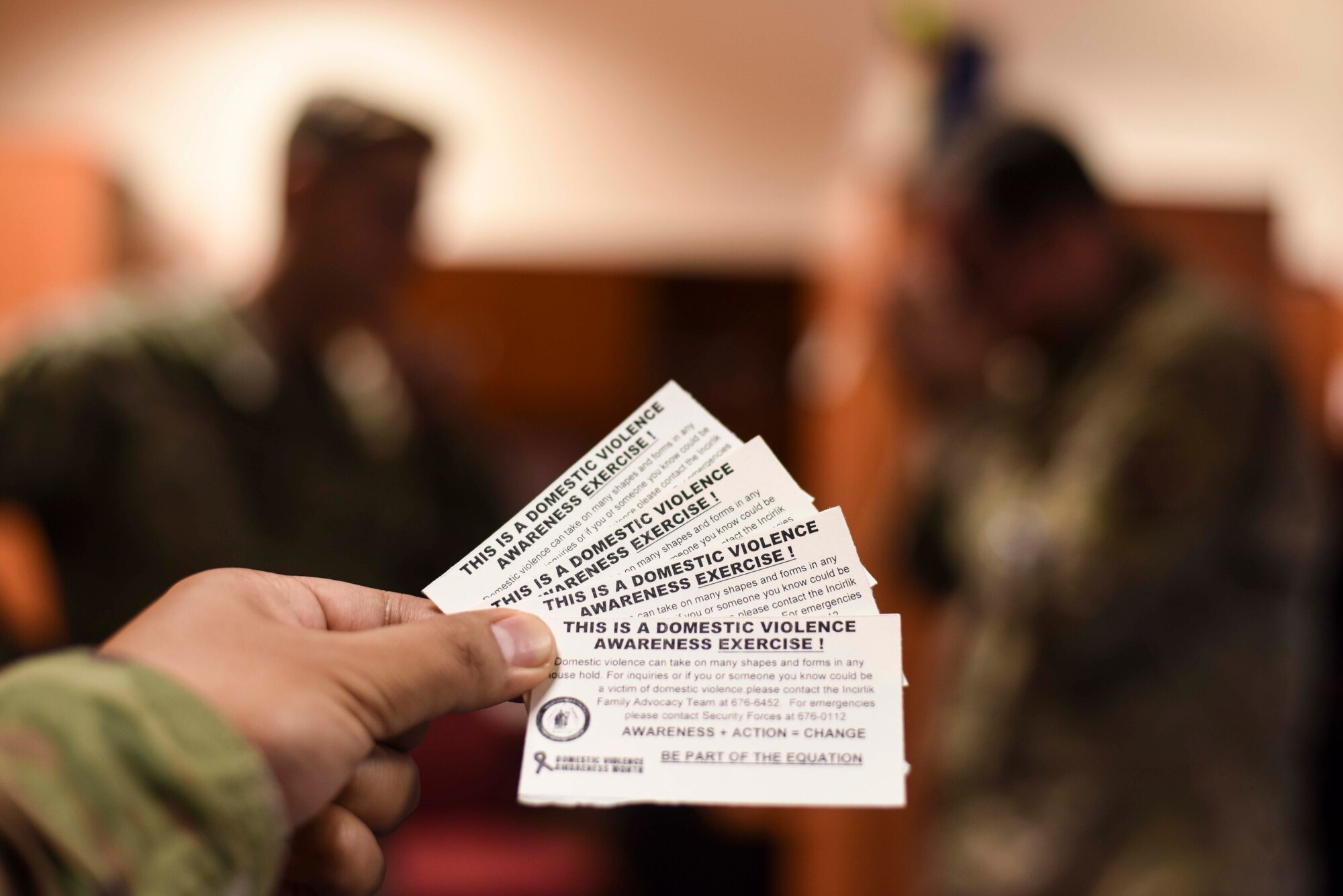 Domestic violence awareness leaflets are seen against a background of two Airmen involved in a simulated intervention Oct. 10, 2019, at Incirlik Air Base, Turkey. The 39th Air Base Wing conducted a domestic violence awareness exercise to initiate responses from bystanders around the installation. (U.S. Air Force photo by Staff Sgt. Joshua Magbanua)