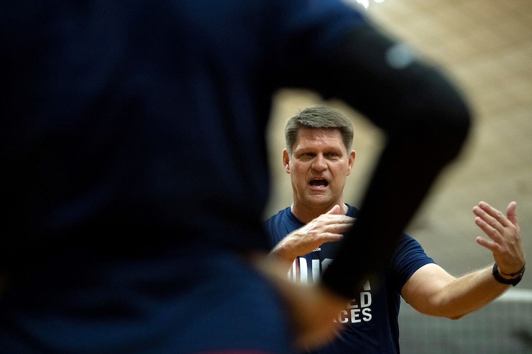 Coach gives instructions to team, his face framed by the arm of a player facing him with her hand on her hip.