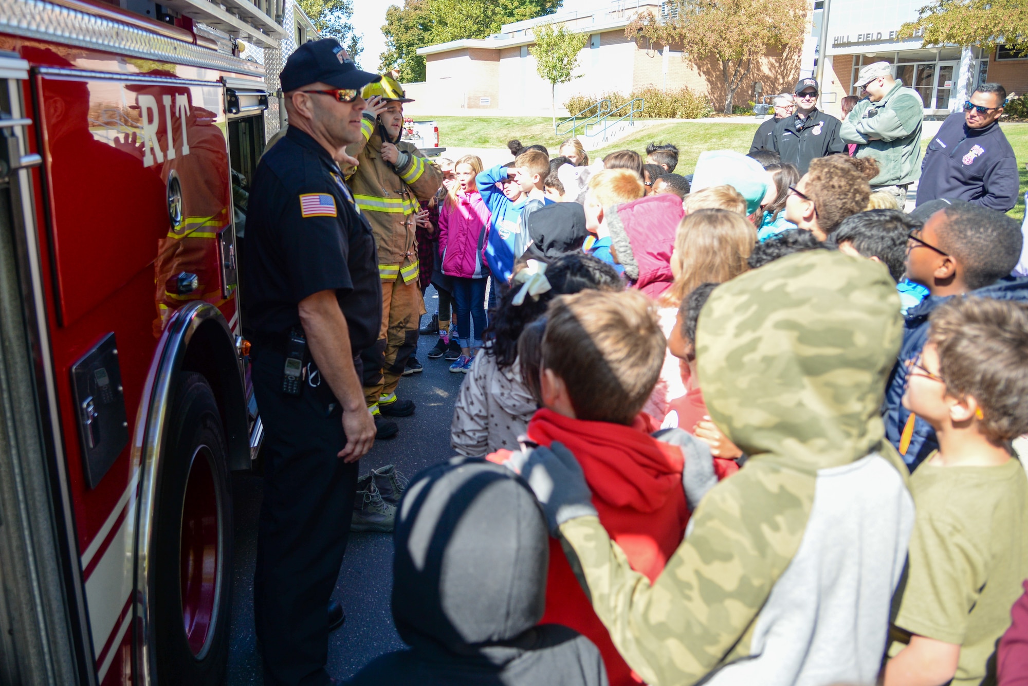 (Left to right) Doran Smith and Airman 1st Class Gabriel Briones, Fire and Emergency Services at Hill Air Force Base, Utah, demonstrate firefighting equipment for Hill Field Elementary students Oct. 10, 2019, in front of the department’s fire engine. This was one of the numerous outreach events base firefighters sponsored for Fire Prevention Week Oct. 6-12. (U.S. Air Force photo by Cynthia Griggs)