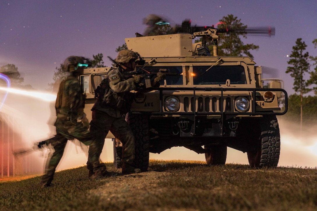 Soldiers stand around a military vehicle pointing their weapons toward a simulated target.
