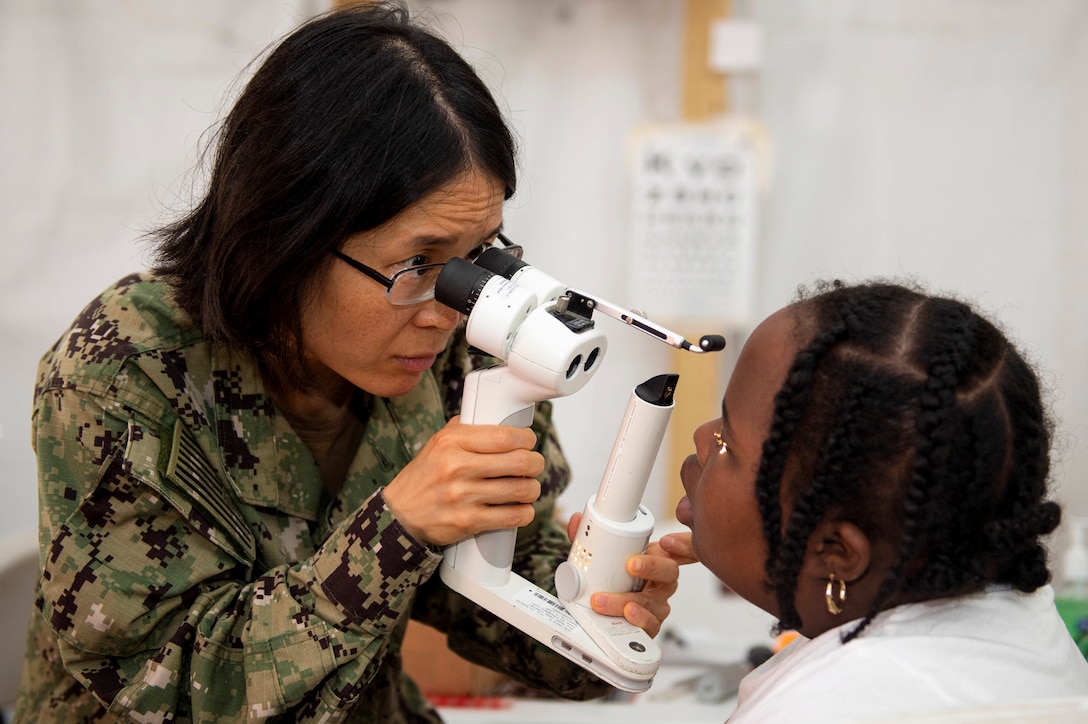 A Navy optometrist uses a medical device to look into a patient's eyes.