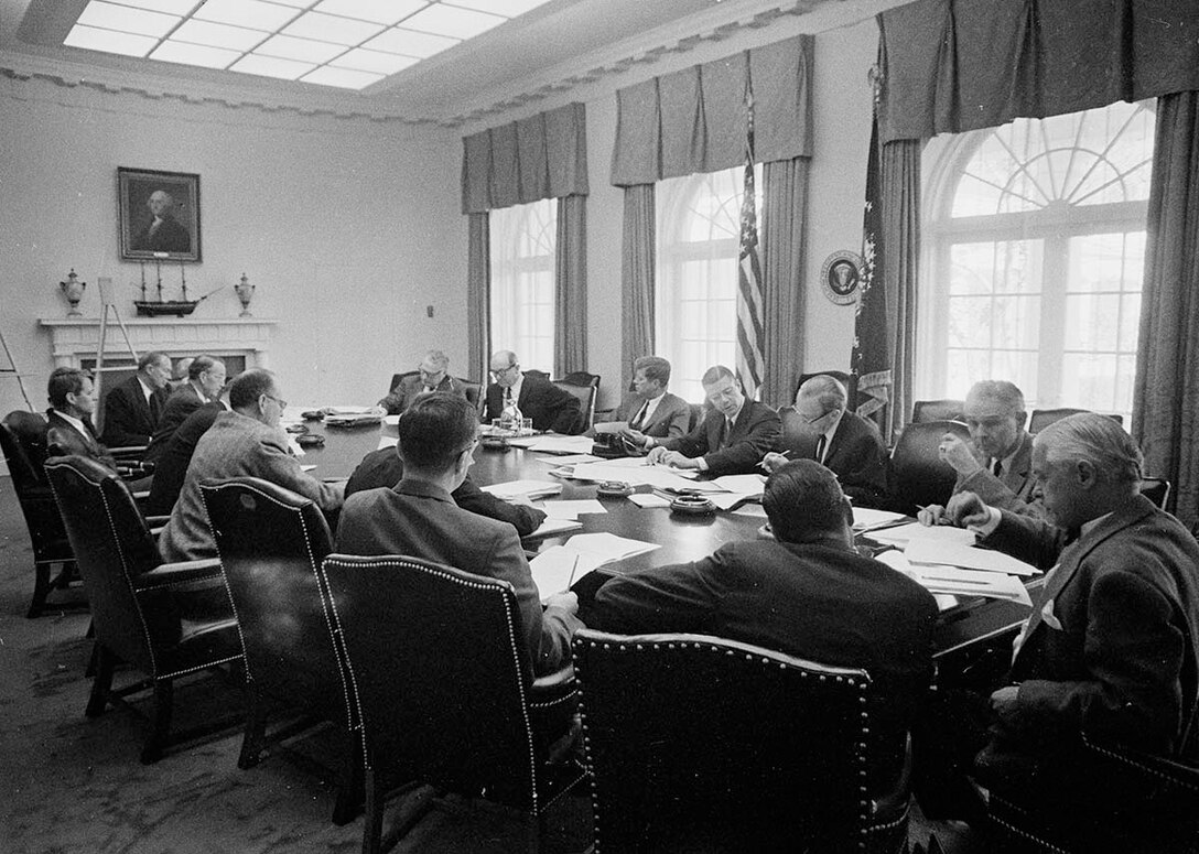 ST-A26-1-62 			29 October 1962 
Meeting of the Executive Committee of the National Security Council (EXCOMM) regarding Cuba in the Cabinet Room, White House, Washington, D.C. Clockwise from top right side of table: Under Secretary of State George Ball; Secretary of State Dean Rusk; President John F. Kennedy; Secretary of Defense Robert S. McNamara; Deputy Secretary of Defense Roswell Gilpatric; Chairman of the Joint Chiefs of Staff General Maxwell Taylor; Assistant Secretary of Defense Paul Nitze; Deputy United States Information Agency  (USIA) Director Donald Wilson; Special Counsel to the President Theodore Sorensen; Special Assistant to the President for National Security McGeorge Bundy; Secretary of the Treasury C. Douglas Dillon; Vice President Lyndon B. Johnson (mostly hidden behind Dillon); Attorney General Robert F. Kennedy; former Ambassador to the Soviet Union Llewellyn Thompson; Arms Control and Disarmament Agency Director William C. Foster; Central Intelligence Agency (CIA) Director John McCone (mostly hidden behind Thompson and Foster).

Please credit "Cecil Stoughton. White House Photographs. John F. Kennedy Presidential Library and Museum, Boston"