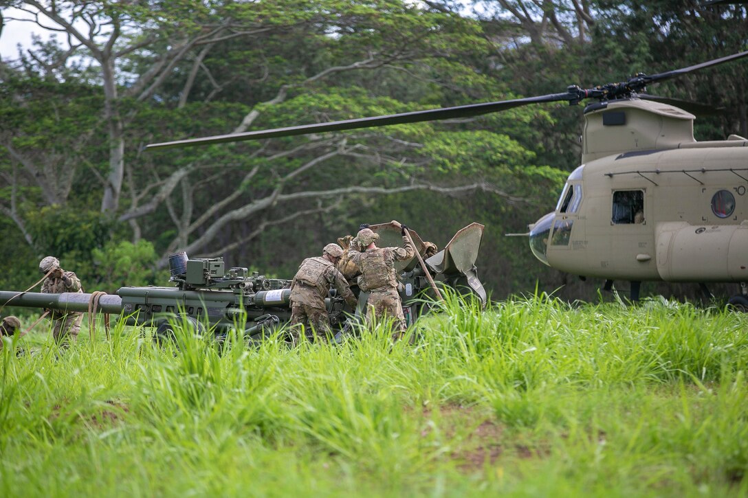 Soldiers work on military equipment next to a helicopter.