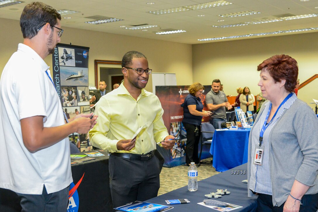 Two men and a woman talk while standing around a table.