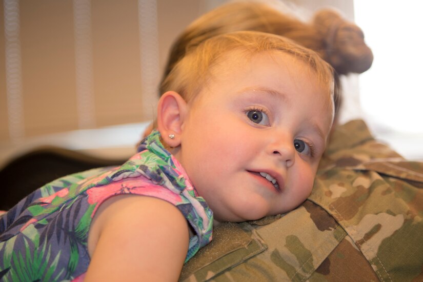 A small child rests her head on a service member’s shoulder.