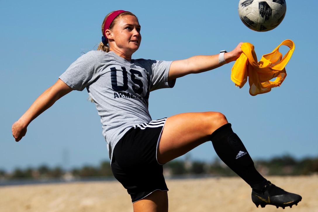 A female military athlete kicks a soccer ball.