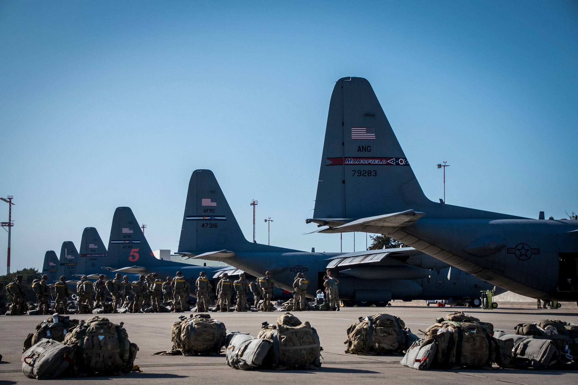 Photo of C-130's sitting on the flight line with troops waiting to board a C-130