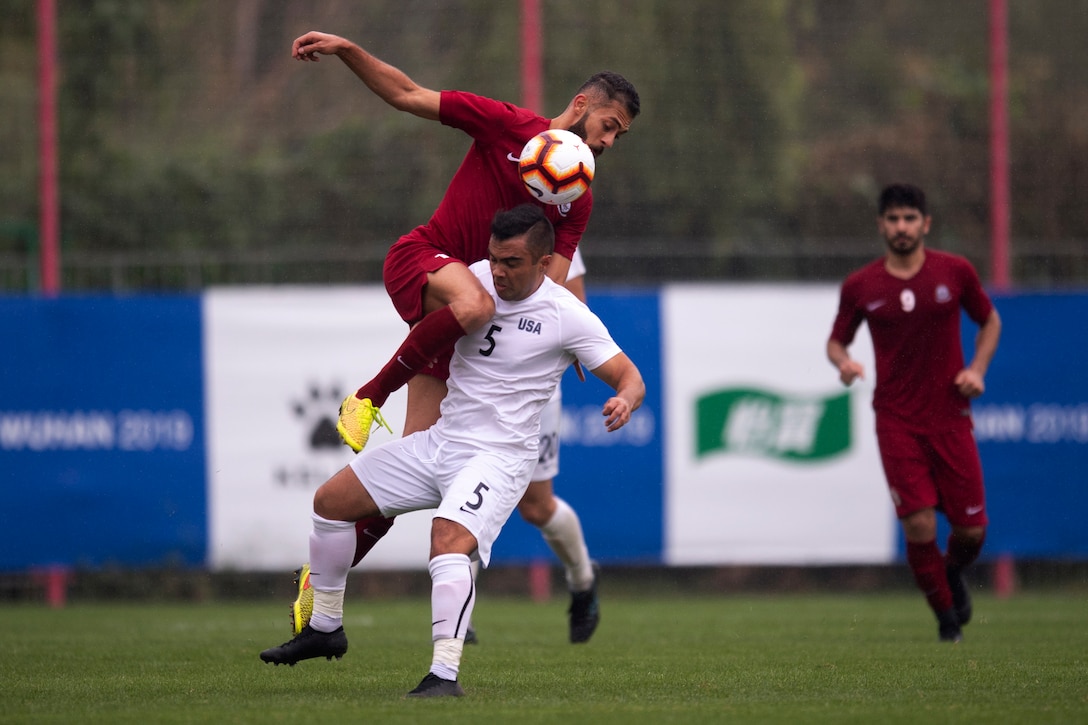 One soccer player jumps on top of another player as they compete for the ball.