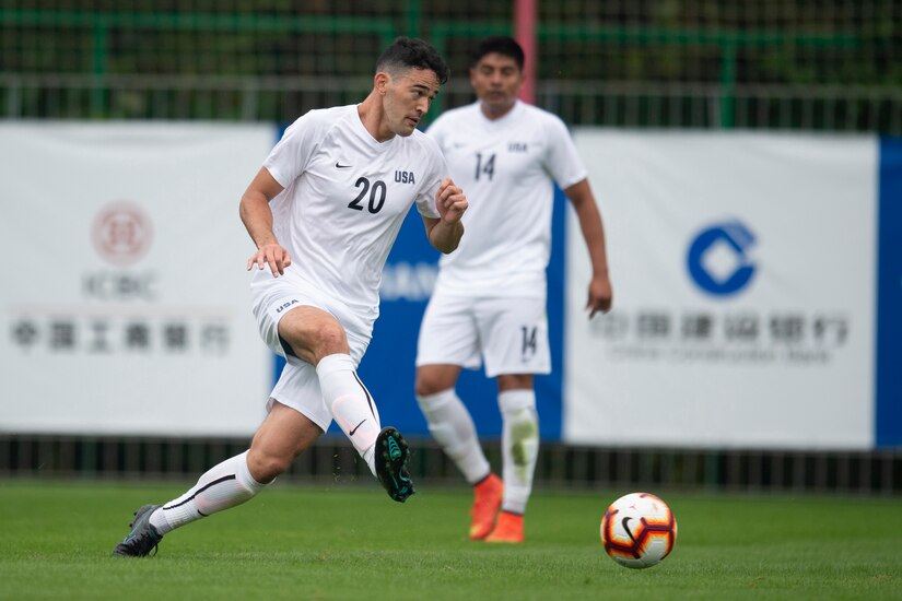A soccer player kicks a ball as another watches in the background.