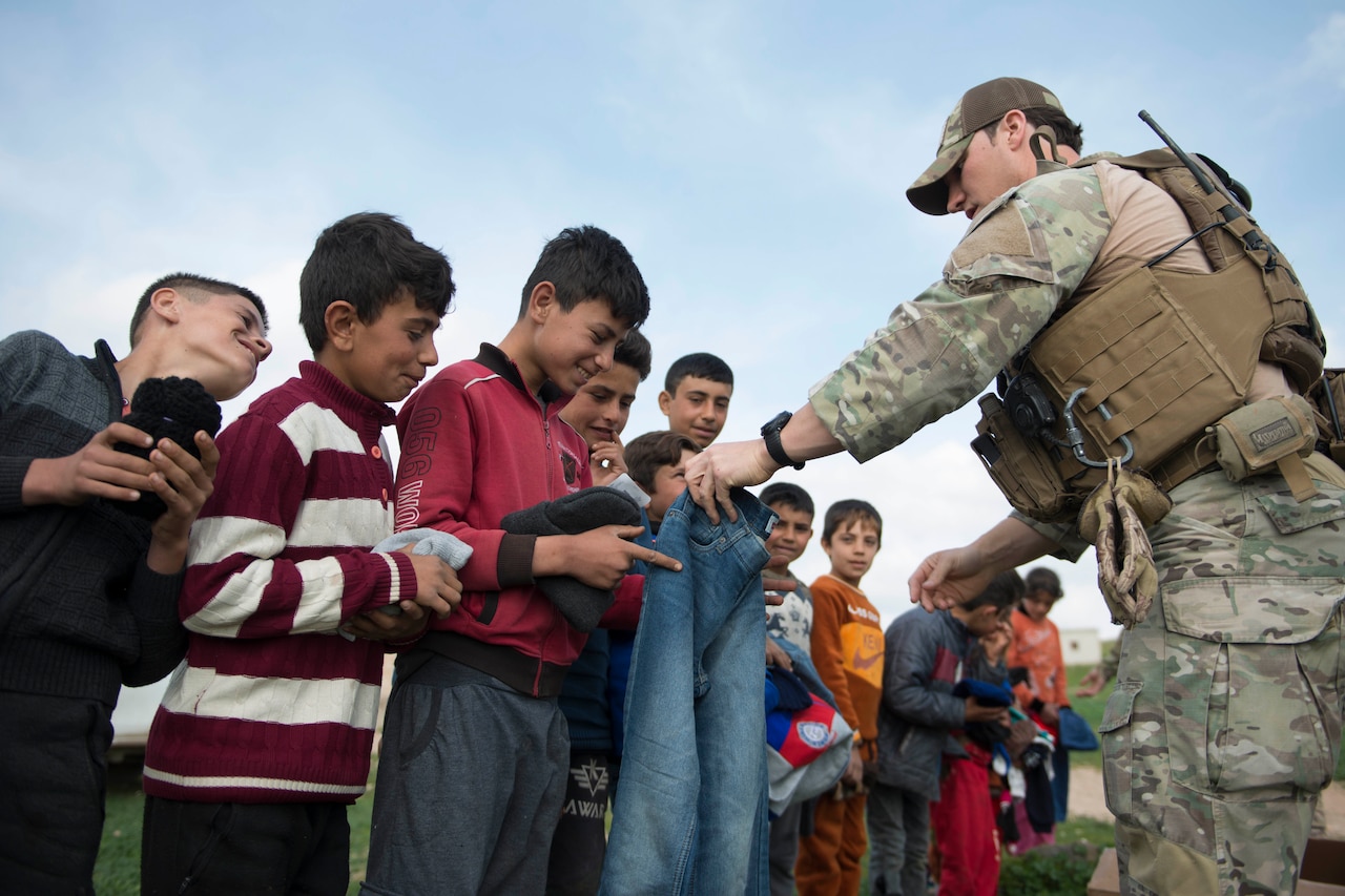 Airmen hands clothes to children.
