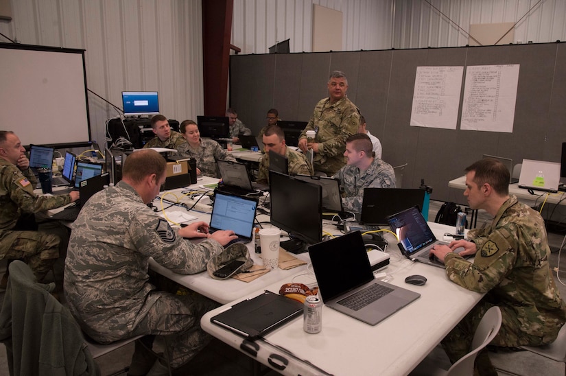 Service members looking at laptops sit around a conference table.