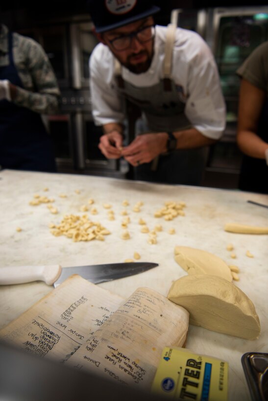 Chef Kevin Scharpf’s, USO Celebrity Chef Tour participant, old notebook sits out to the semolina dough recipe as team Chop It Like It’s Hot prepares the pasta for their dish during a cooking competition Oct. 15, 2019, at F.E. Warren Air Force Base, Wyo. 15 Airmen from the 90th Force Support Squadron food operations were split into three teams and partnered with a celebrity chef during the competition for mentorship. (U.S. Air Force photo by Senior Airman Abbigayle Williams)