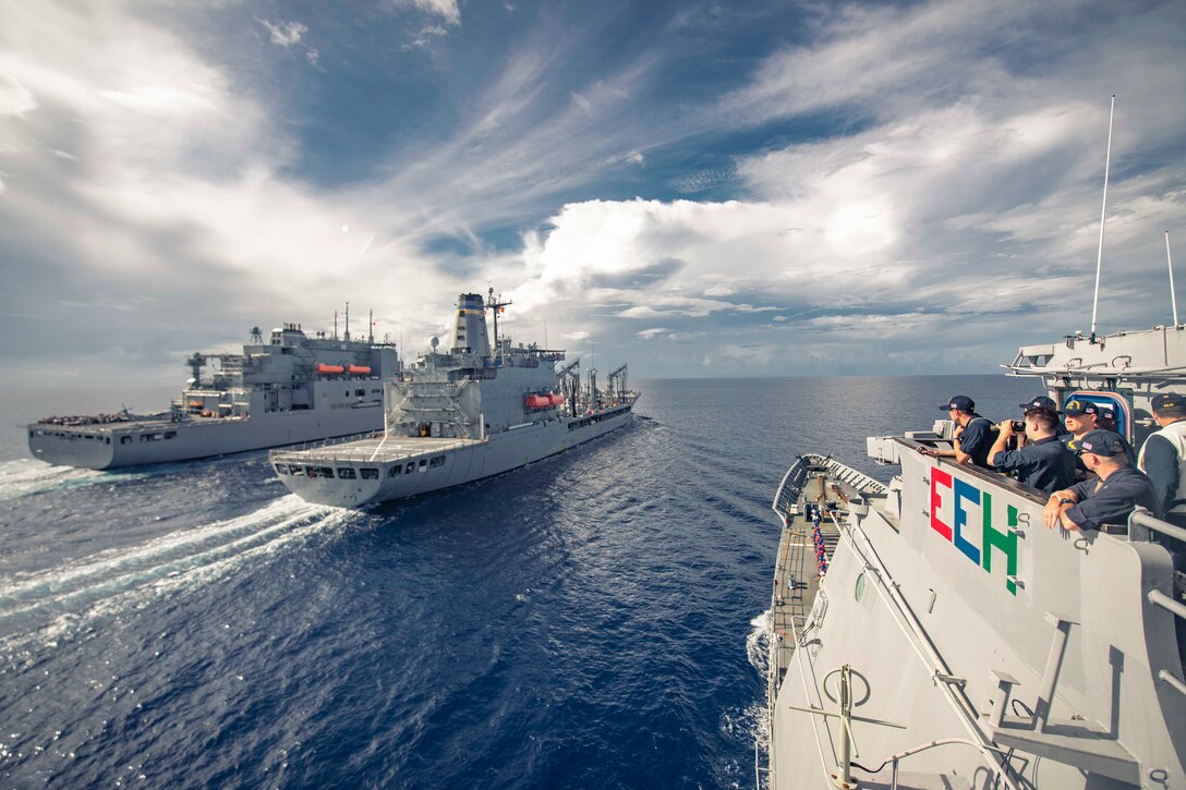 Three ships travel in blue waters, one slightly behind and away from  the other two.