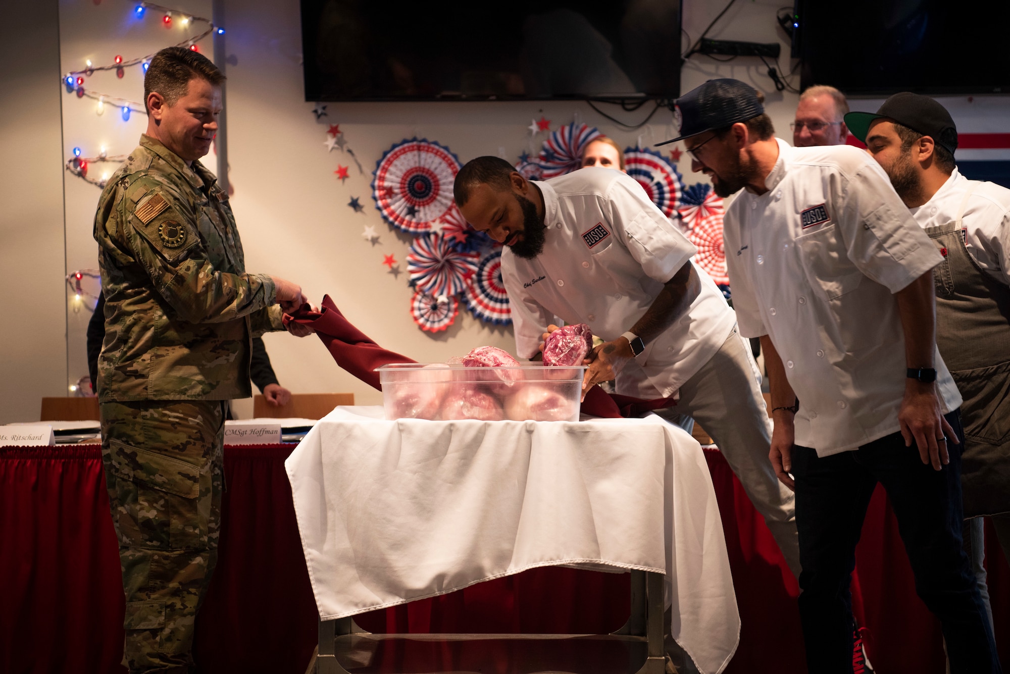 Colonel Peter Bonetti, 90th Missile Wing commander, uncovers the mystery ingredient, lamb, as the celebrity chef mentors looks on, before the chef competition begins Oct. 15, 2019, at F.E. Warren Air Force Base, Wyo. The USO partnered with three chefs from Bravo’s season 16 “Top Chef” to bring morale on military instillations and hold cooking competitions. (U.S. Air Force photo by Senior Airman Abbigayle Williams)