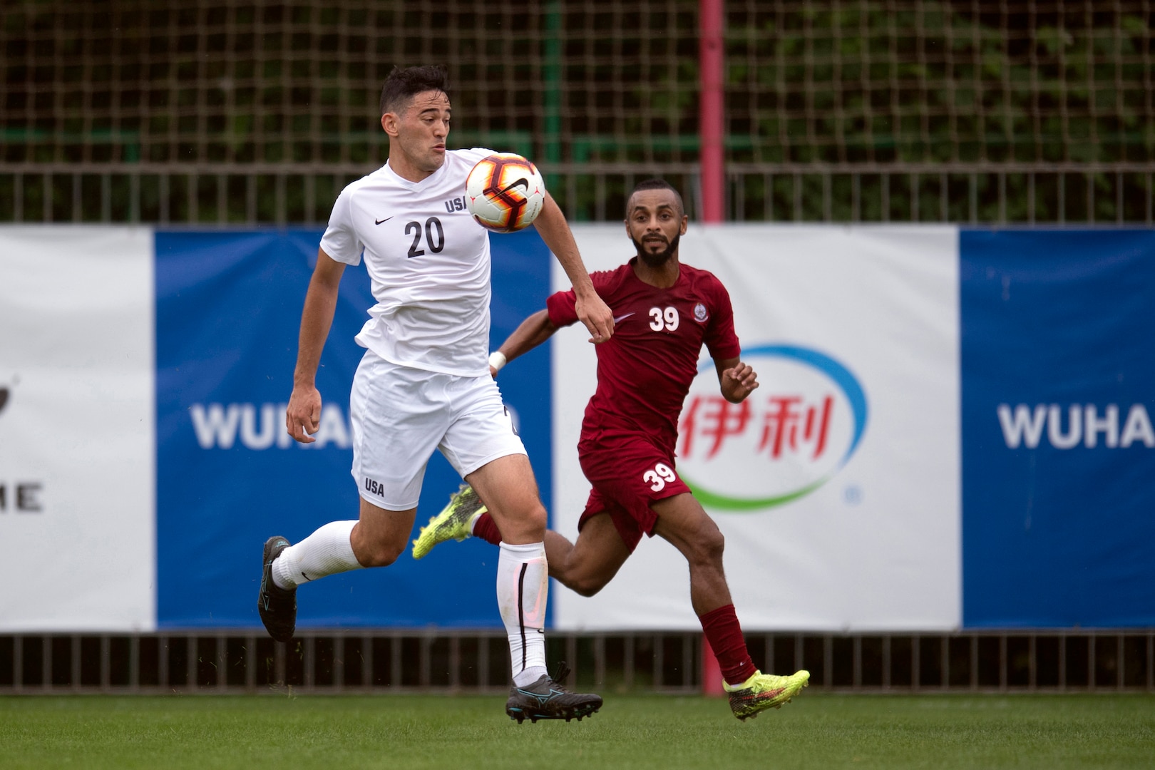 A Navy athlete runs as a soccer ball rebounds off his chest as another player runs behind him.