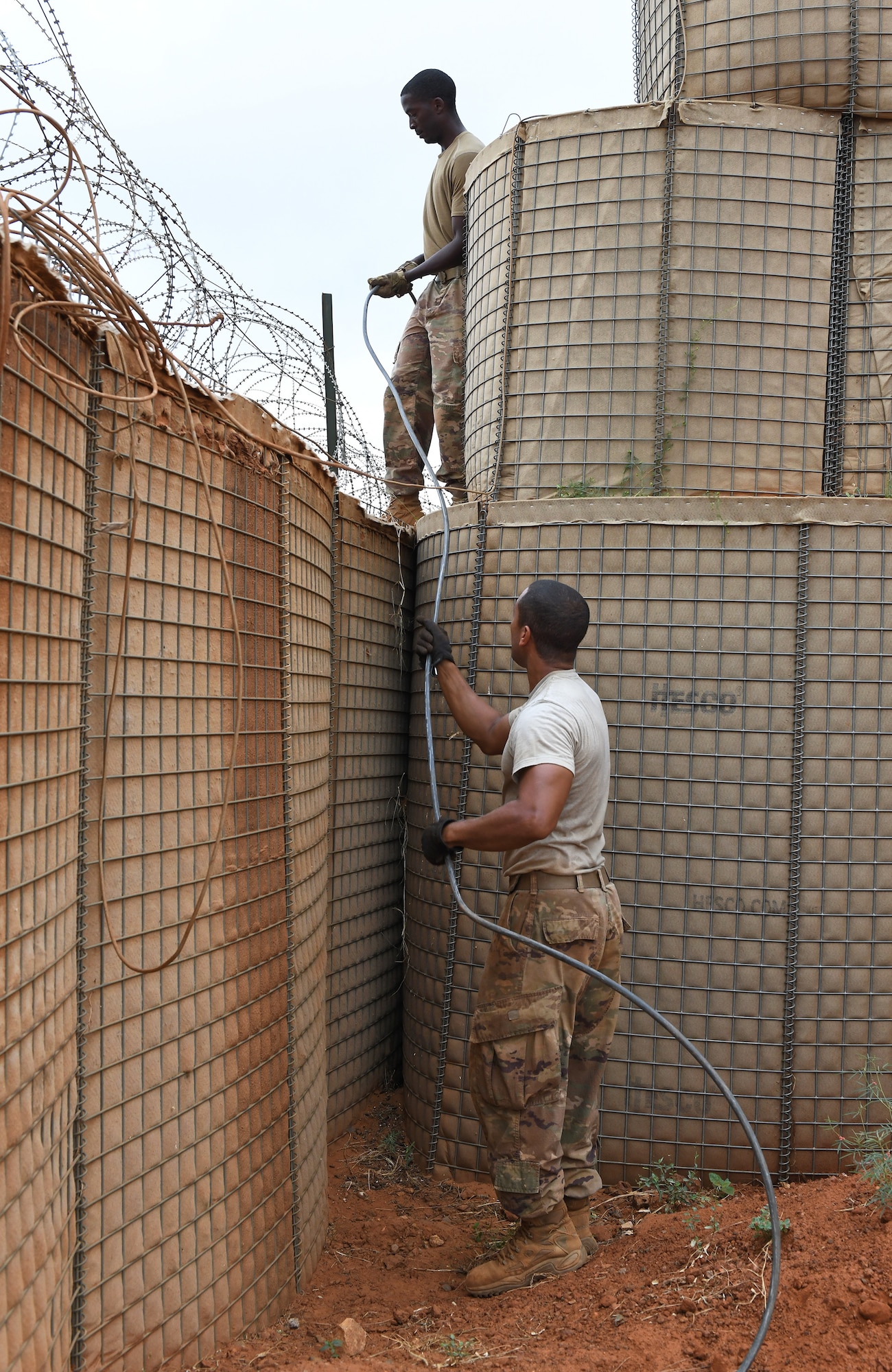 U.S. Air Force Tech. Sgt. Guillermo Cajigas, 768th Expeditionary Air Base Squadron Power Production and Electrical Systems section lead (bottom), and SSgt Jeremy Davis, 768th EABS Electrical Systems craftsman (top), run a cable for perimeter lighting at Nigerien Air Base 101, Niamey, Niger, Oct. 10, 2019. The cable was rerouted to make way for the foundation of the base’s new gym facilities. (U.S. Air Force photo by Staff Sgt. Alex Fox Echols III)