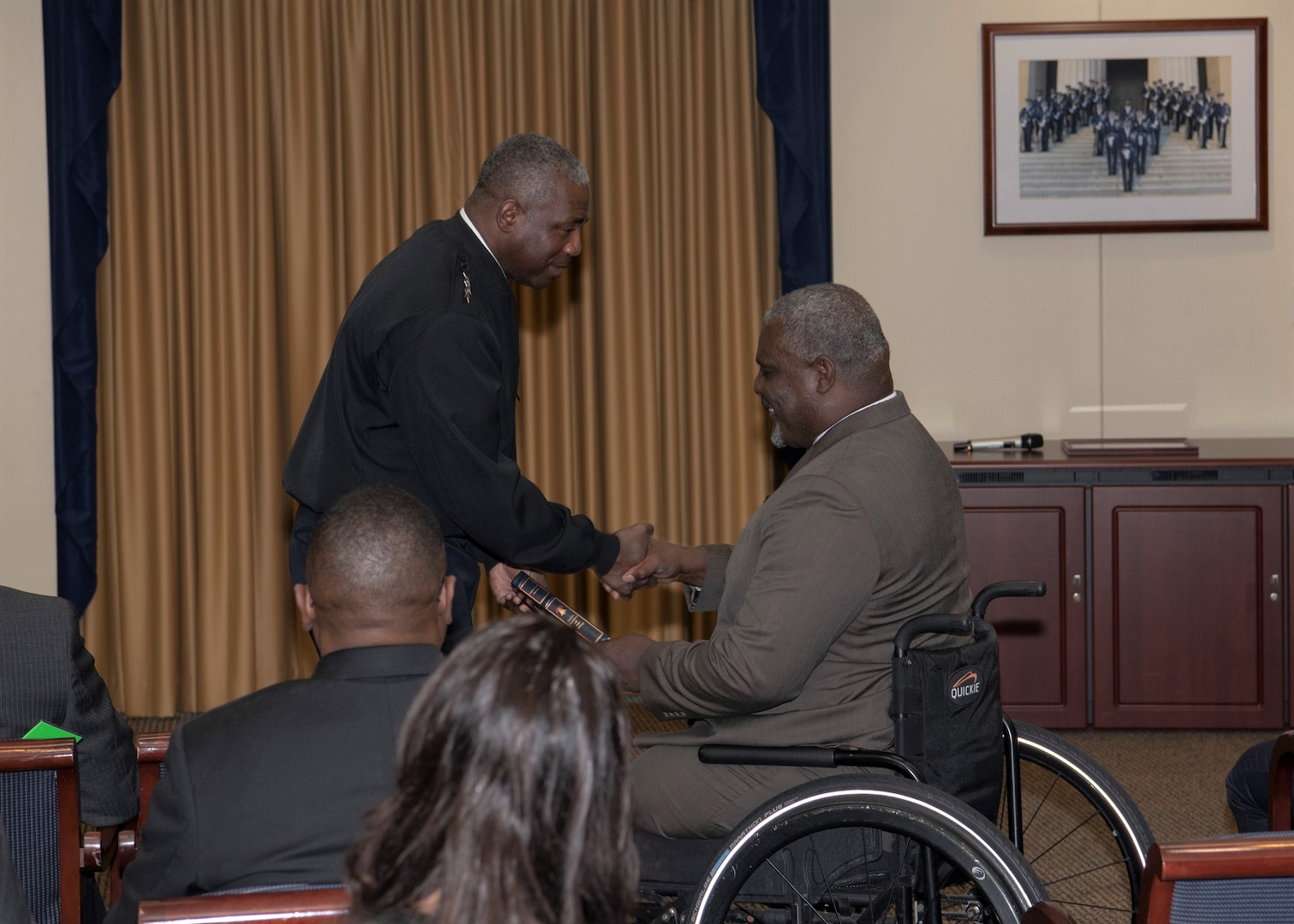 One man presents a book to another man in wheelchair.