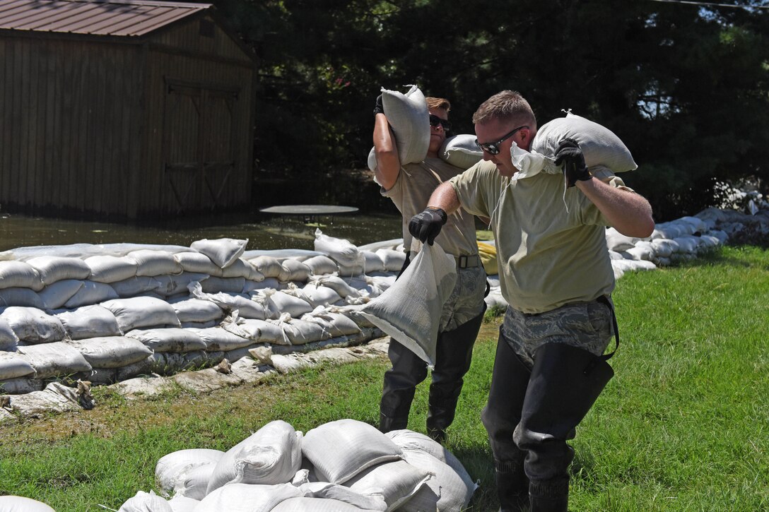 Two men carry sandbags.