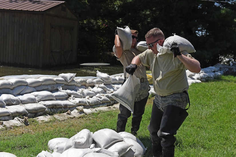 Two men carry sandbags.