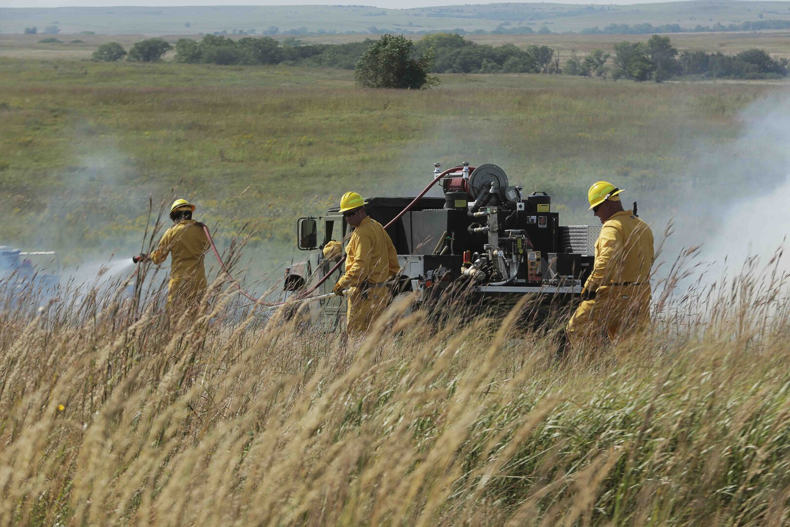 A group of Soldiers and Airmen from the Kansas National Guard spray flames with water from a High Mobility Multipurpose Wheeled Vehicle (HMMWV) during an integrated exercise with civilian fire departments at the Smokey Hill Range in Salina, Kansas, Sept. 19, 2019.